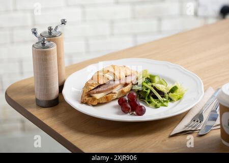 Panino con croissant appena sfornato ripieno di prosciutto e formaggio, servito su un piatto bianco con un lato di insalata verde mista e qualche uva rossa. Foto Stock