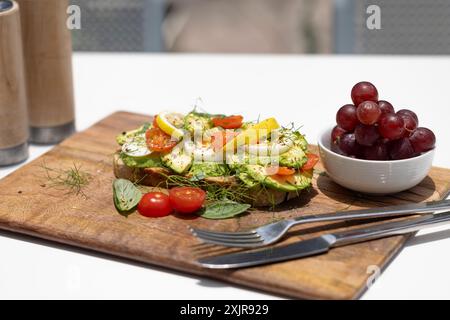 Un delizioso piatto da colazione con uova in camicia, toast all'avocado con limone e pomodoro, un'insalata fresca e un piccolo mucchio di uva. Foto Stock