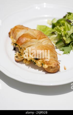 Colazione a buffet con croissant ripieni di uova strapazzate ed erbe aromatiche, servita con un contorno di insalata su un piatto bianco. Foto Stock