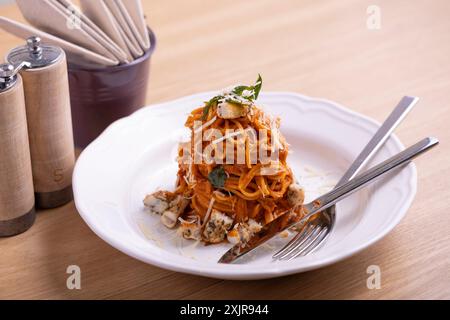 Una torre di spaghetti splendidamente placcata ricoperta da una ricca salsa di pomodoro, guarnita con foglie di basilico fresco e condita con formaggio grattugiato. Foto Stock