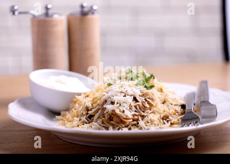 Una foto ravvicinata di un piatto di biryani profumati guarniti con erbe fresche, serviti con un lato di cremosa salsa di yogurt. Foto Stock