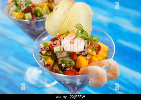 Insalata di ceviche con gamberetti, mango e avocado in un recipiente di vetro su sfondo blu. Cibo latino-americano. Deliziosa ceviche di gamberi appena sfornata. Gamberetti ma Foto Stock