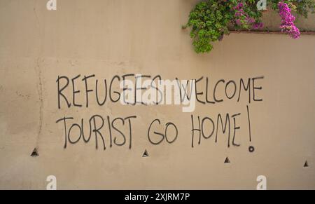 Barcellona, Spagna. Graffiti su un muro che dice "i rifugiati sono i benvenuti. I turisti tornano a casa!" Foto Stock