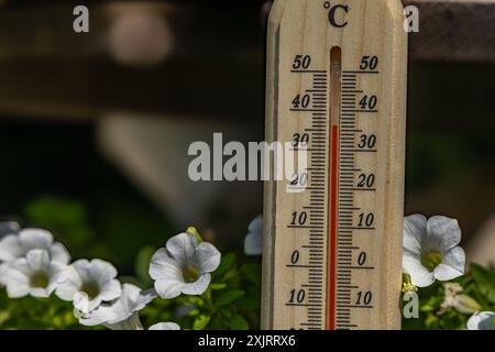 Un uomo tiene in mano un termometro di legno in giardino che indica una temperatura molto elevata - protezione contro il calore Foto Stock