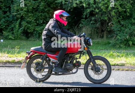 Milton Keynes, Regno Unito - 18 luglio 2024: Uomo in sella a una Yamasaki F66-50 rossa del 2023 su una strada di campagna britannica Foto Stock