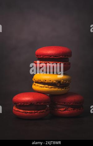 Uno shot ravvicinato di quattro macaron impilati uno sopra l'altro. I macaron sono disposti in uno schema di rosso, giallo e rosso. Sono contrapposti a Foto Stock