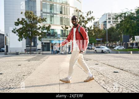 Felice giovane uomo nero con le cuffie che ascolta la musica che cammina per la strada della città. Foto Stock