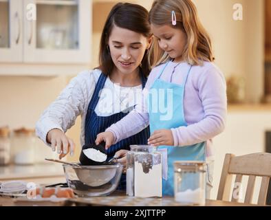 Mamma e figlia felici e cuocere con farina in cucina per dessert, snack o mescolare gli ingredienti a casa. Un bambino o una bambina che aiutano Foto Stock