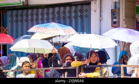 Folle di persone usano gli ombrelli per proteggersi dal sole caldo Foto Stock