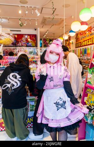 Bella giovane donna giapponese che indossa la maschera facciale e vestito in costume rosa e nero del negozio Candy ago-go, in posa e sventolando allo spettatore. Foto Stock