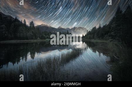 Le stelle si snodano su un paesaggio pittoricamente maestoso che si riflette in un lago, con montagne sullo sfondo. Foto naturalistiche a lunga esposizione con astrofotografia Foto Stock