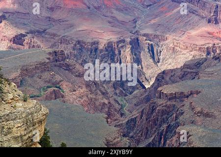 Ampia vista con uno scorcio luminoso del fiume Colorado alla base delle colorate pareti del canyon del Grand Canyon, sotto ombre variopinte indotte da paesaggi nuvolosi Foto Stock