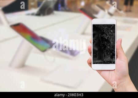 tenere a mano il telefono cellulare con schermo in vetro rotto e negozio elettronico di sfocatura astratta per la riparazione dello smartphone Foto Stock