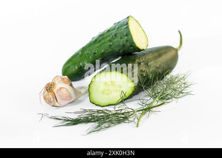 Due cetrioli interi e un cetriolo a fette con uno spicchio di aglio e un rametto di aneto su una superficie bianca. Foto Stock