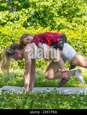 Una giovane madre atletica va a fare sport, yoga all'aperto con suo figlio. Il bambino siede sul retro della madre stile di vita attivo. Esercizio fisico. Foto Stock