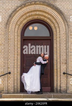 Lo sposo tiene la sposa tra le braccia e si guarda con tenerezza. Sullo sfondo di una grande porta marrone. Tenerezza, amore, relazioni, Foto Stock