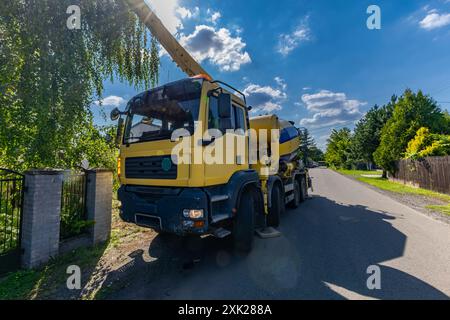 Una grande betoniera nera e gialla mescola e versa cemento mentre costruisce le fondamenta di una casa Foto Stock