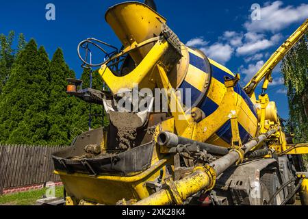 Una grande betoniera nera e gialla mescola e versa cemento mentre costruisce le fondamenta di una casa Foto Stock