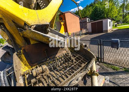 Una grande betoniera nera e gialla mescola e versa cemento mentre costruisce le fondamenta di una casa Foto Stock