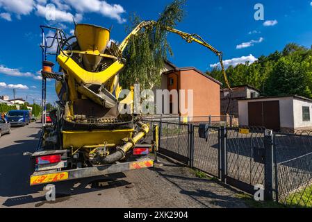 Una grande betoniera nera e gialla mescola e versa cemento mentre costruisce le fondamenta di una casa Foto Stock
