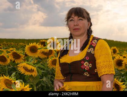 Una donna è in piedi in mezzo a un campo con molti girasoli gialli. Capelli intrecciati, vestiti con abiti nazionali tedeschi, camicetta gialla, pondr marrone Foto Stock