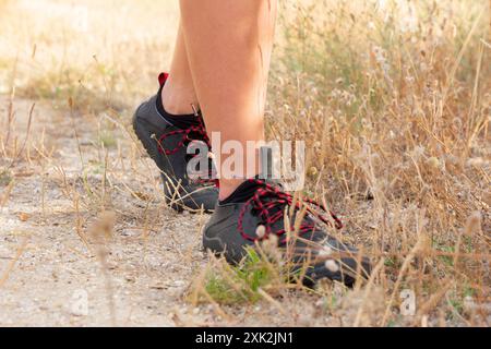 Questa immagine cattura una vista ravvicinata dei piedi rivestiti di stivali robusti, camminando con attenzione lungo un sentiero asciutto e erboso nella campagna indicata dal paesaggio Foto Stock