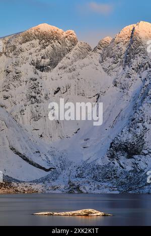 Una splendida mattina invernale a Lofoten, Norvegia, con luce del sole dorata che illumina le vette delle montagne ricoperte di neve, riflesse sulle tranquille acque Foto Stock