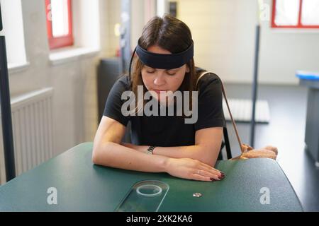 Una giovane donna siede a un tavolo con una fascia sensore che misura l'attività cerebrale. Concetto di scienza applicata nella vita reale Foto Stock