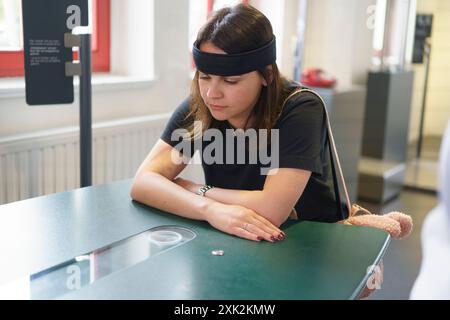 Una giovane donna siede a un tavolo con una fascia sensore che misura l'attività cerebrale. Concetto di scienza applicata nella vita reale Foto Stock