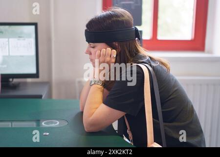 Una giovane donna siede a un tavolo con una fascia sensore che misura l'attività cerebrale. Concetto di scienza applicata nella vita reale Foto Stock