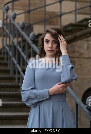 una giovane ragazza con i capelli scuri in un abito grigio si trova vicino ai fiori bianchi di rododendro. Voltato aggraziatamente Foto Stock