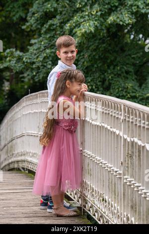 Ridendo, allegro, felice adolescente e ragazza in piedi su un ponte bianco nel parco. Fratello e sorella. La ragazza guarda in lontananza con curiosit Foto Stock