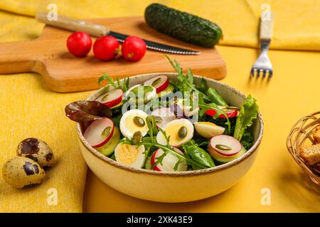 Ciotola di sana insalata verde con uova di quaglia, ravanello e rucola su sfondo giallo, primo piano Foto Stock