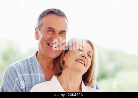 Ritratto, abbraccio e accappatoio con coppia anziana, amore e sostegno nel soggiorno di casa insieme. Sorridi, faccia e fiducia con un uomo felice e maturo e. Foto Stock