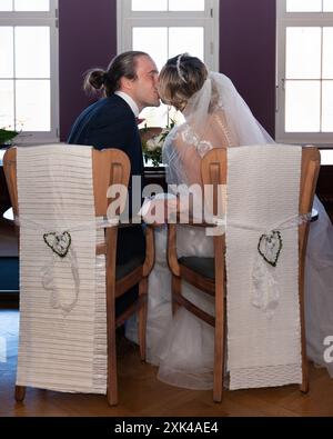 Bacio di una coppia dopo il matrimonio. La sposa e lo sposo si siedono sulle sedie e si baciano teneramente Foto Stock