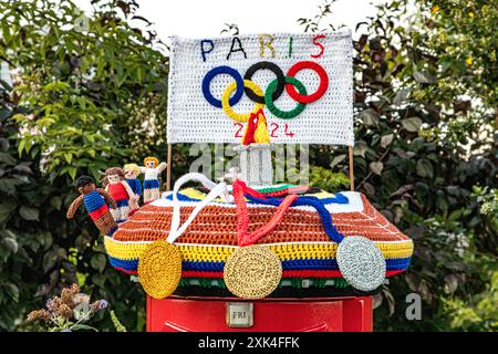 Colorato top in scatola per posta a maglia che celebra le Olimpiadi di Parigi 2024 con medaglie all'uncinetto, atleti, fiamma e anelli olimpici, Weymouth, Dorset Foto Stock