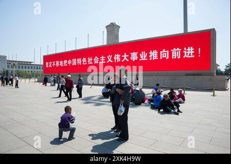 Cina, Pechino, 13 aprile 2012. I cinesi in una piazza con un pannello a LED acceso in rosso con uno slogan in cinese che promuove la causa del socialismo Foto Stock