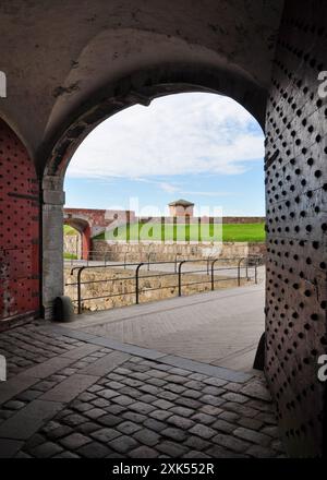 Porte rivettate rosse all'ingresso di un vecchio forte. Porte in legno con borchie e rivetti in metallo invecchiato. Cortile del castello sullo sfondo. Foto Stock