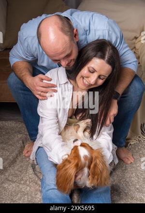 Famiglia felice con un cane. Una donna tiene tra le braccia il Cavalier King Charles Cocker Spaniel e ride allegramente, un uomo guarda con tenerezza l'animale Foto Stock