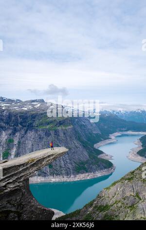 Un'escursione solitaria sulla scogliera di Trolltunga in Norvegia ammira l'aspra bellezza delle montagne e dei fiordi che si estendono sotto, Trolltunga, Norvegia, mentre le donne asiatiche hanno visitato la Trolltunga Foto Stock