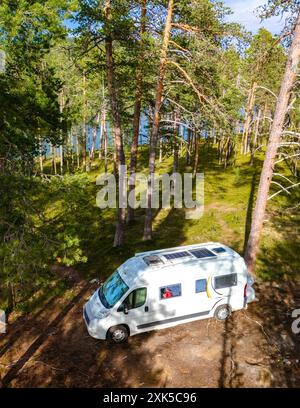 Un camper bianco parcheggiato in una radura nella foresta finlandese della Lapponia, con il sole che splende tra gli alberi. Foto Stock