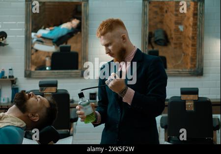 I parrucchieri lavorano per un bel ragazzo al barbiere. Balm su parti del corpo asciutte per idratare la pelle. Baffi cera. Crema per la rasatura in legno di sandalo Foto Stock