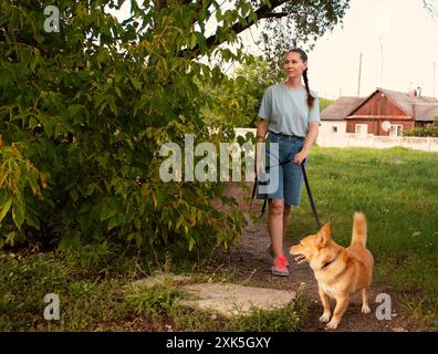 una donna guida il suo cane rosso al guinzaglio in una passeggiata d'estate. Un'alleanza tra un cane e un umano Foto Stock