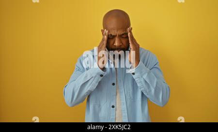 Bel giovane afroamericano con una barba in piedi su un isolato sfondo giallo sopra il muro, che sembra stressato con le mani sui templi. Foto Stock