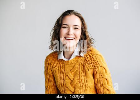 Giovane donna sorridente con capelli ricci. Affascinante giovane donna con capelli ricci, sorridente e che guarda la fotocamera. Trasuda positività e gioia, in piedi Foto Stock