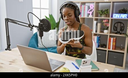 La donna afroamericana con trecce che indossano abbigliamento sportivo tiene la sneaker in studio radiofonico Foto Stock