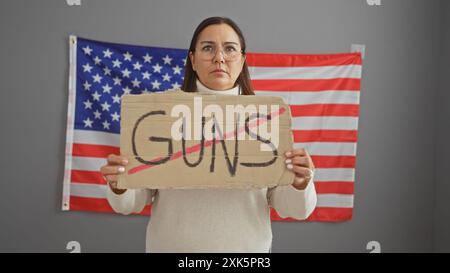 Una donna ispanica seria ha un segno di protesta contro le armi di fronte alla bandiera americana Foto Stock