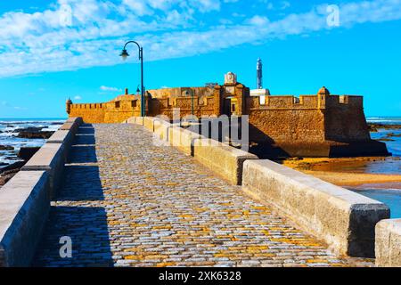 La passerella in pietra conduce al Castillo de San Sebastian a Cadice, Spagna. La fortezza è circondata dall'acqua e ha un faro. La passerella è fatta di ciottoli Foto Stock
