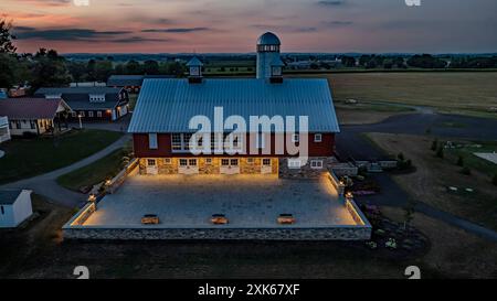 Ronks, Pennsylvania, USA, 19 luglio 2024 - tranquilla fattoria al tramonto con Un grande fienile rosso con Un Silo bianco, un cortile in pietra illuminato, Una vicina Brick House e ampi campi verdi sotto Uno splendido cielo al tramonto, creando Un ambiente tranquillo e pittoresco. Foto Stock