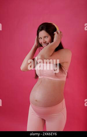 donna incinta in abiti da ginnastica che ascolta musica con le cuffie Foto Stock